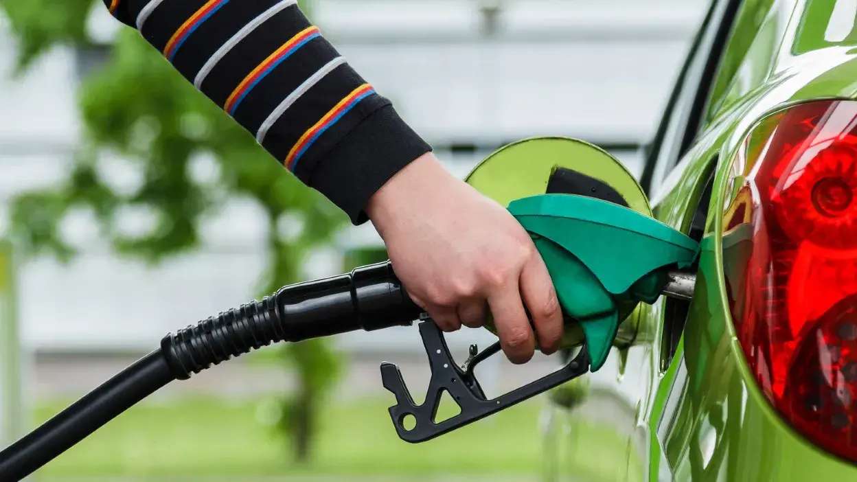 Mão a segurar bico de combustível verde a abastecer carro verde.