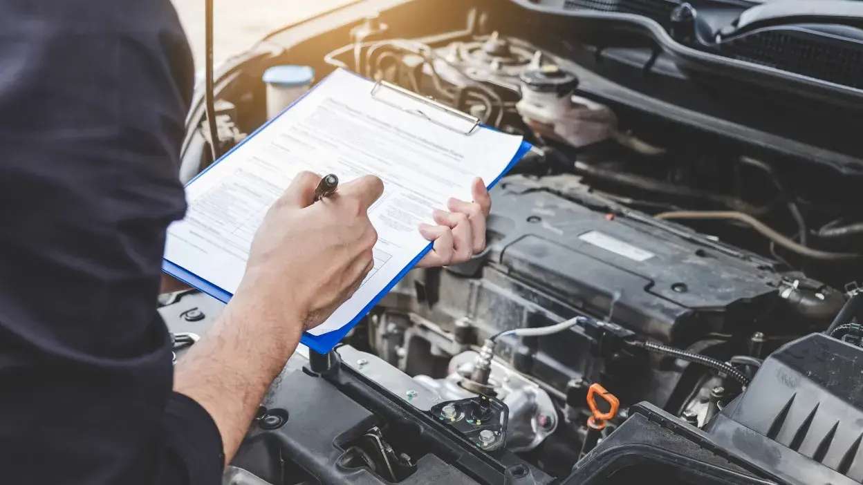 Pessoa a preencher formulário durante inspeção ao motor de um carro aberto