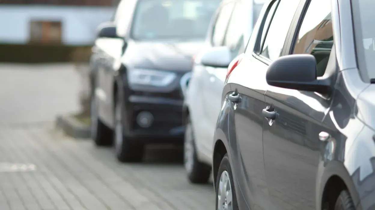Carros estacionados em fila numa rua com calçada de paralelos.