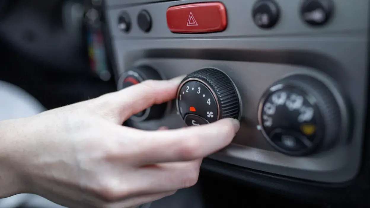 Mão a ajustar o botão do ventilador no painel de controlo do ar condicionado de um carro