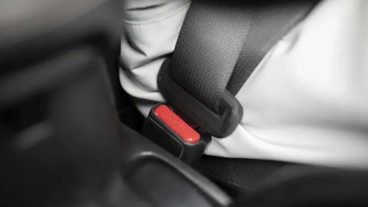 Pessoa a usar cinto de segurança dentro de um carro, com foco na fivela do cinto.