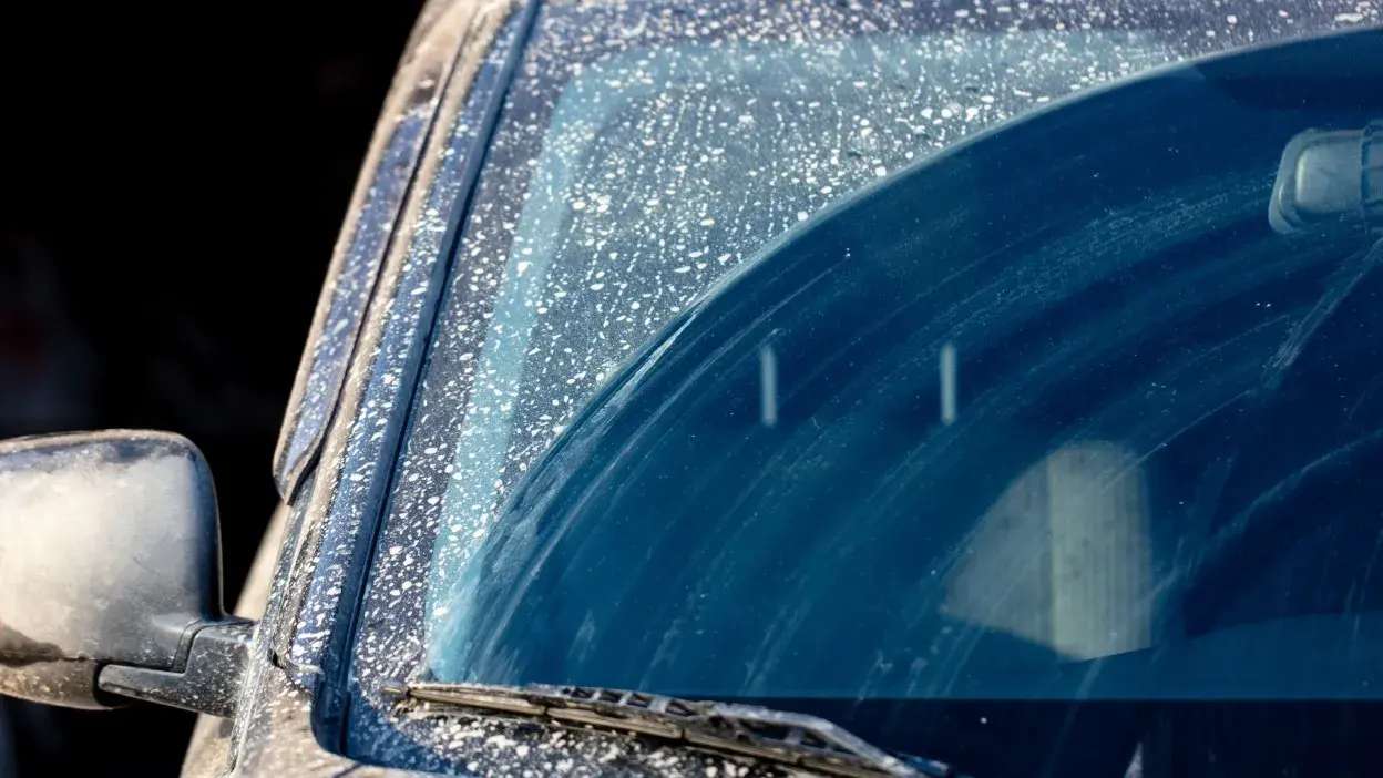 Para-brisas de carro coberto de pó e sujidade com limpa-vidros visível.