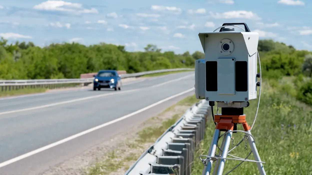 Radar de velocidade montado numa berma de estrada com carro ao fundo