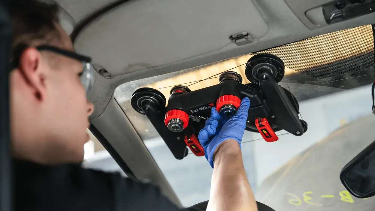 Técnico a instalar um para-brisas com ferramenta de sucção dentro de um carro.