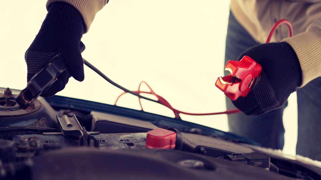 Mãos a segurar nos cabos para ligar a bateria do carro