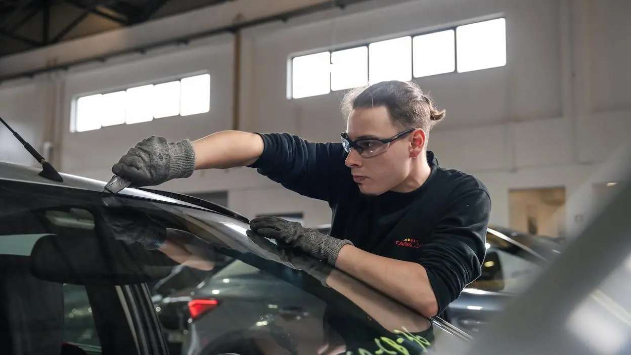 Técnico automóvel a reparar ou substituir o para-brisas de um veículo numa oficina.